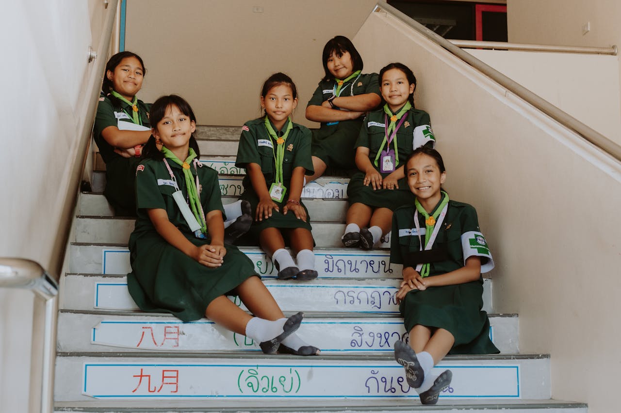Smiling schoolgirls in uniform sitting together on stairway indoors, showing unity and friendship.